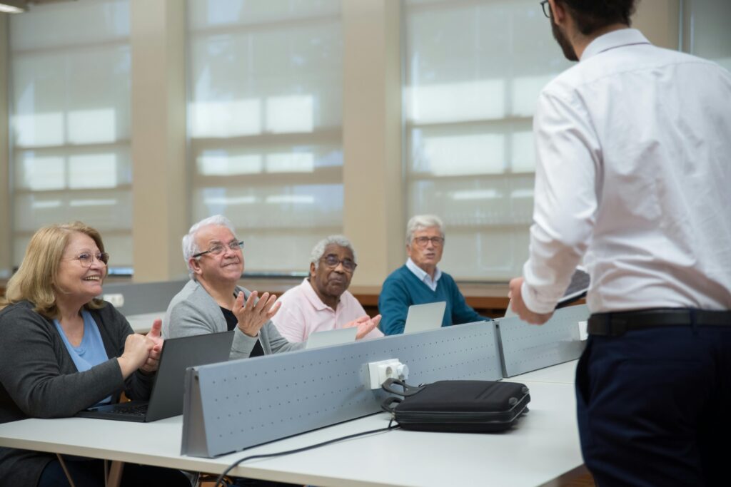 pexels-photo-7983565-7983565 Senior adults attend a computer class, led by an instructor, in a classroom setting.